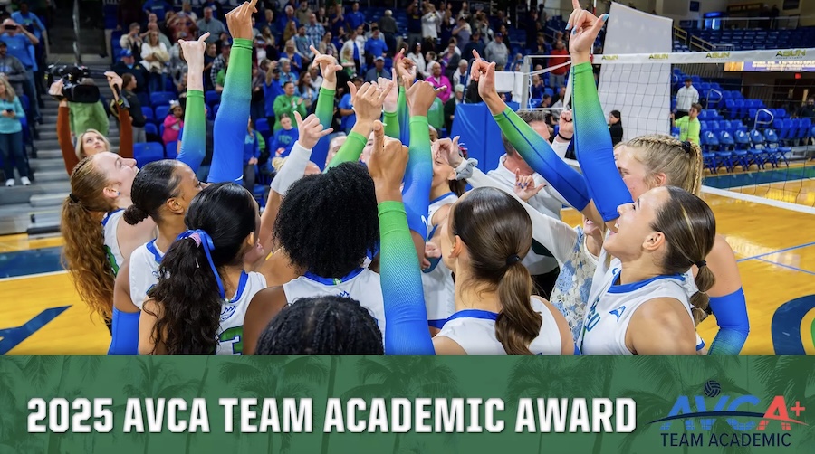 FGCU women's volleyball team huddles on the court with hands raised in unity, wearing white jerseys with blue and green accents. A volleyball net and spectators are visible in the background. The bottom portion of the image has the words ‘2025 AVCA Team Academic Award’ with a green background that has a palm tree pattern. 