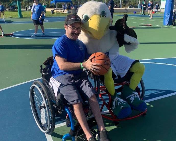 Image of disabled student in wheelchair next to Azul- school mascot, holding a basketball and wings up sign